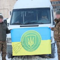 на фото двоє військових стоять біля спецтранспорту і тримають Прапор України