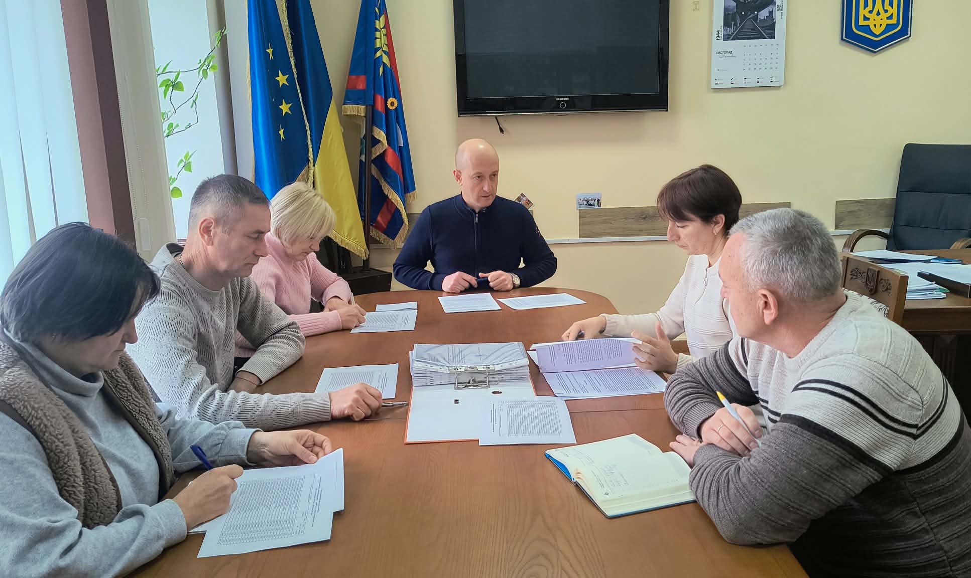 Члени комісії сидят в кабінеті за робочим столом перед ними лежать документи