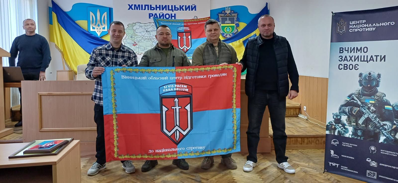 Публічні службовці тримають у руках розгорнутий прямокутний прапор комунальної установи