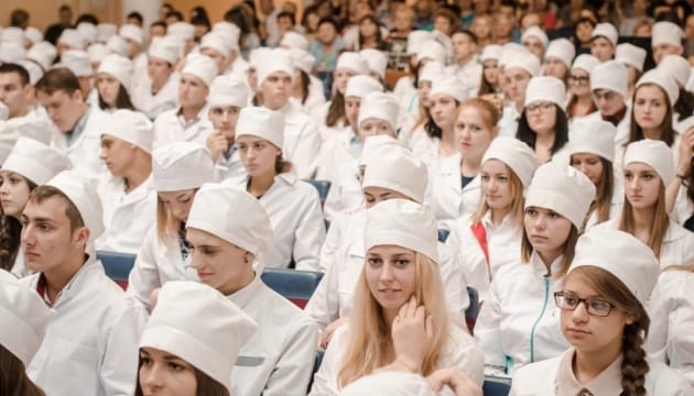 Група людей у білих халатах сидить у великому залі.