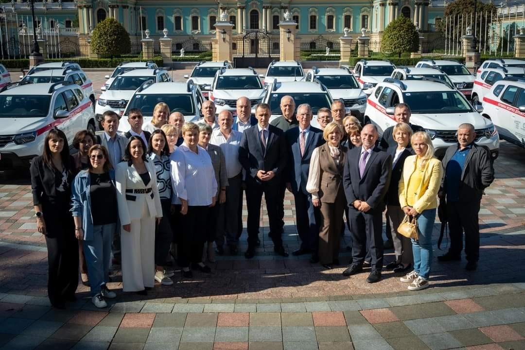 Група людей стоїть перед автомобілями.