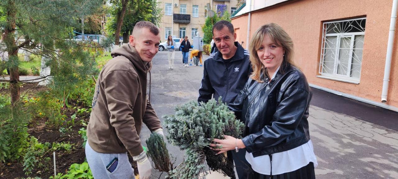 Три людини тримають рослину, оточені зеленню та природою.