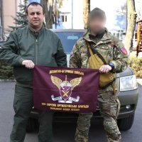 Начальник ОВА Сергій Борзов та військовй тримають у руках прапор із логотипом бригади