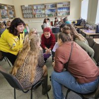 Група людей сидить колом у залі, беручи участь у дискусії чи тренінгу