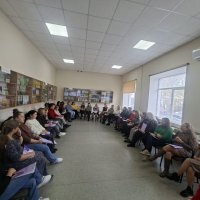 Група людей сидить колом у залі, беручи участь у дискусії чи тренінгу